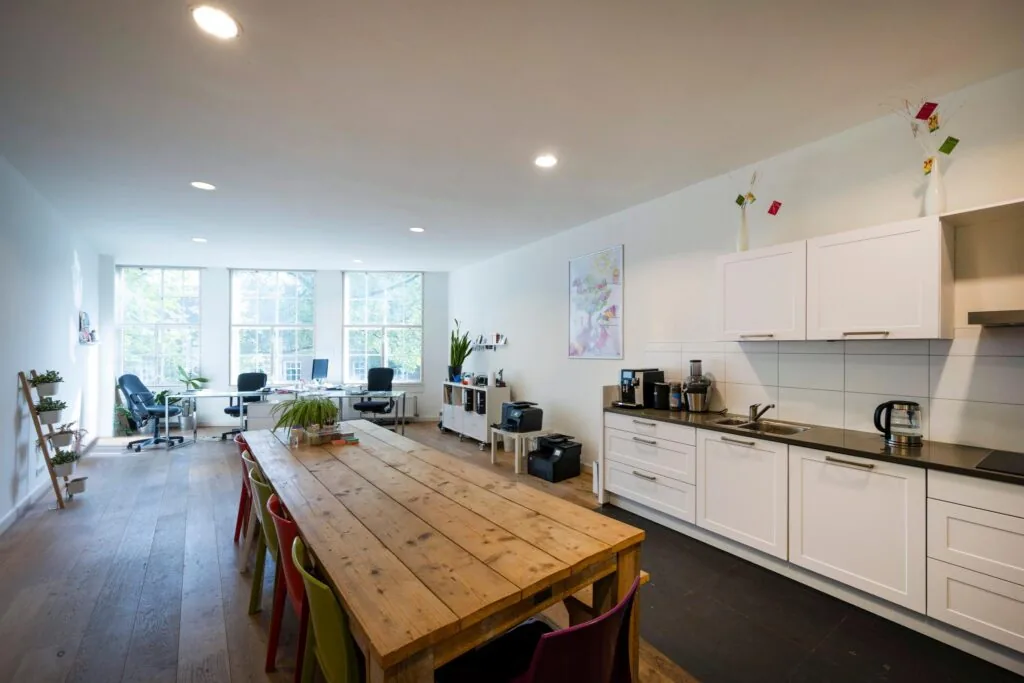 Moderne en lichte kantoorruimte aan de Nieuwezijds Voorburgwal met een lange houten tafel, keukenblok en werkplekken bij grote ramen.